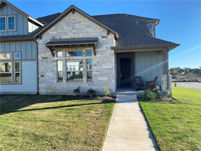 view of front of home featuring a shingled roof, a front lawn, board and batten siding, and stone siding