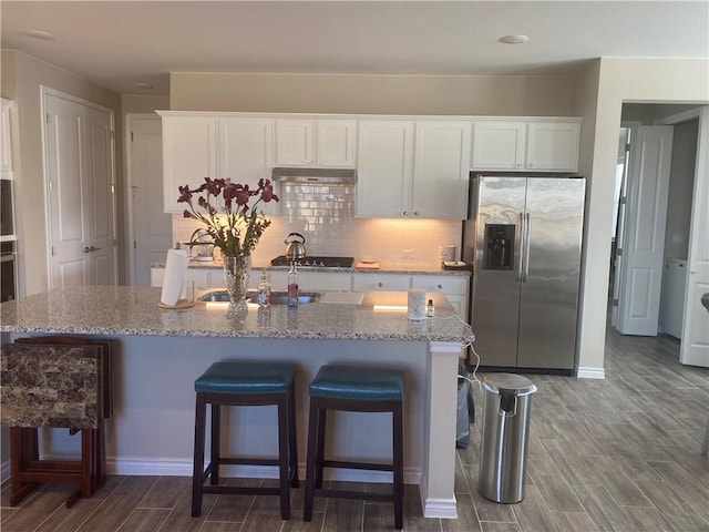 kitchen with appliances with stainless steel finishes, under cabinet range hood, dark wood-style flooring, and white cabinetry
