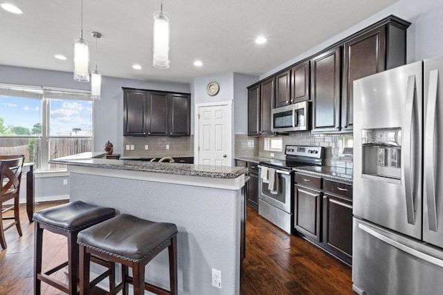 kitchen featuring dark wood finished floors, backsplash, dark brown cabinetry, and stainless steel appliances