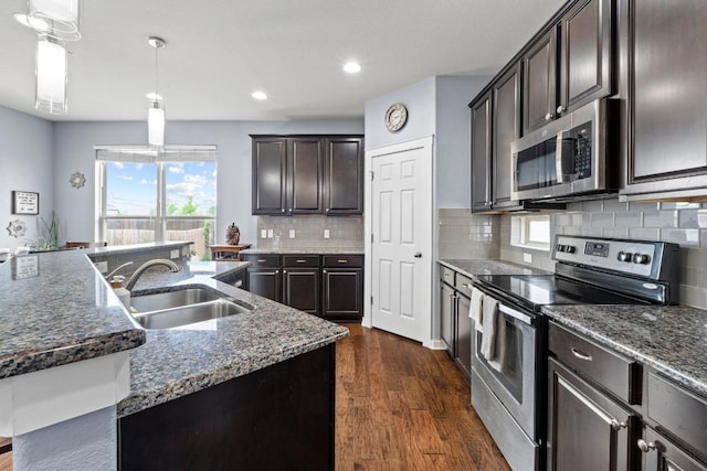 kitchen featuring dark wood-type flooring, a sink, dark stone countertops, and stainless steel appliances
