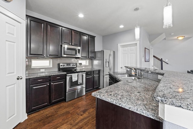kitchen featuring backsplash, dark wood-style flooring, appliances with stainless steel finishes, a sink, and light stone counters