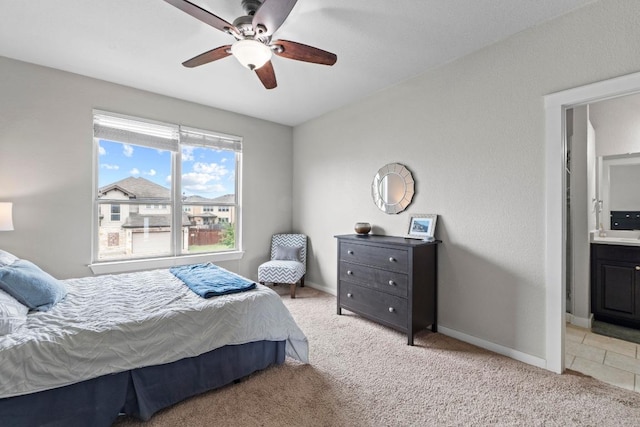 bedroom featuring a ceiling fan, baseboards, light carpet, and ensuite bathroom