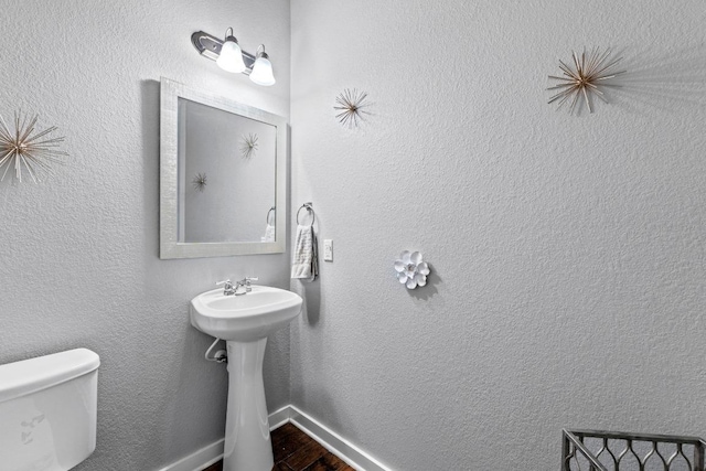 half bath with toilet, baseboards, a sink, and wood finished floors