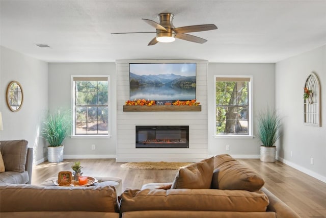 living room featuring plenty of natural light, a large fireplace, ceiling fan, and wood finished floors