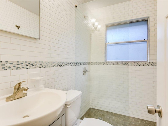 bathroom with vanity, a tile shower, toilet, and tile walls
