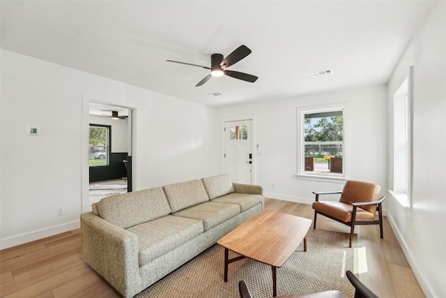 living room featuring visible vents, a ceiling fan, baseboards, and light wood-type flooring