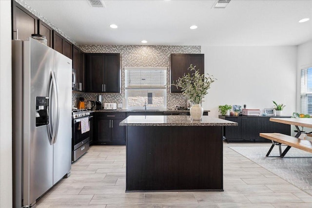 9015 Looksee Ln, Austin, TX 78744 - kitchen with dark brown cabinetry, a kitchen island, dark stone counters, a sink, and stainless steel appliances
