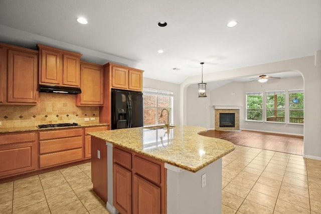 kitchen featuring black fridge, a sink, arched walkways, light tile patterned floors, and under cabinet range hood