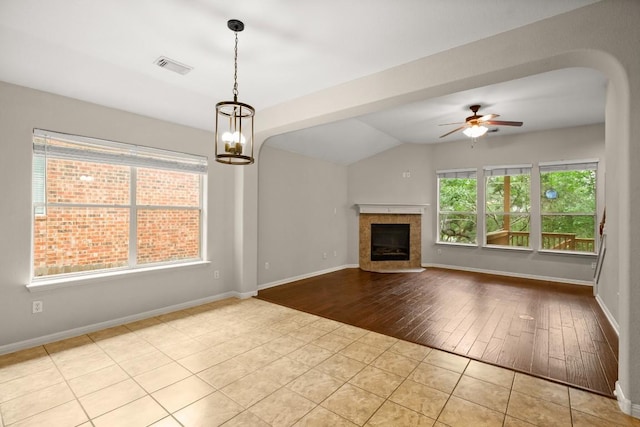 unfurnished living room with tile patterned flooring, visible vents, lofted ceiling, a tile fireplace, and ceiling fan with notable chandelier