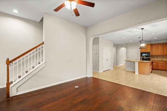 unfurnished living room with a ceiling fan, arched walkways, light wood-type flooring, baseboards, and recessed lighting