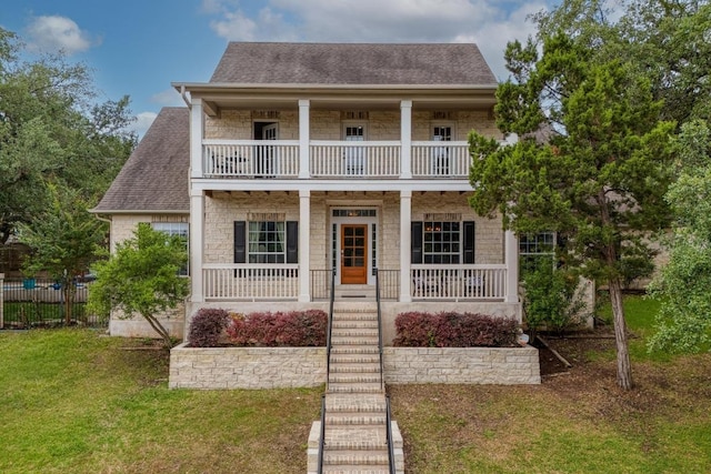 view of front of property featuring covered porch, roof with shingles, a front yard, a balcony, and stone siding