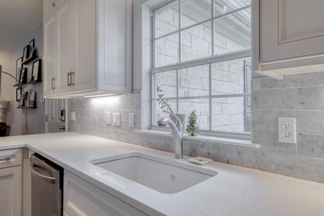 kitchen with stainless steel dishwasher, light stone countertops, white cabinets, tasteful backsplash, and a sink