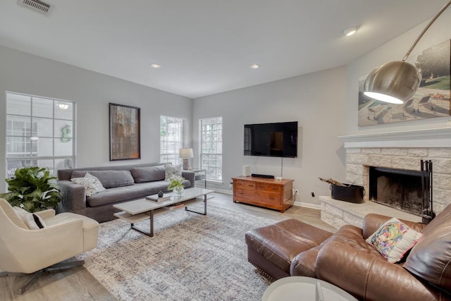 living area featuring visible vents, wood finished floors, baseboards, a stone fireplace, and recessed lighting