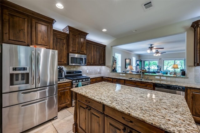 kitchen featuring light stone countertops, ceiling fan, a sink, backsplash, and stainless steel appliances