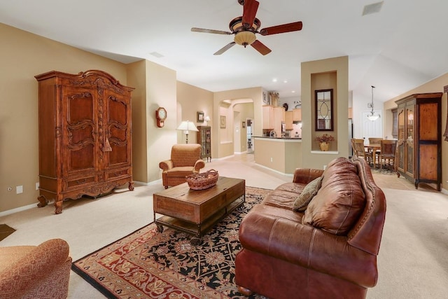 living area with baseboards, a ceiling fan, arched walkways, and light carpet