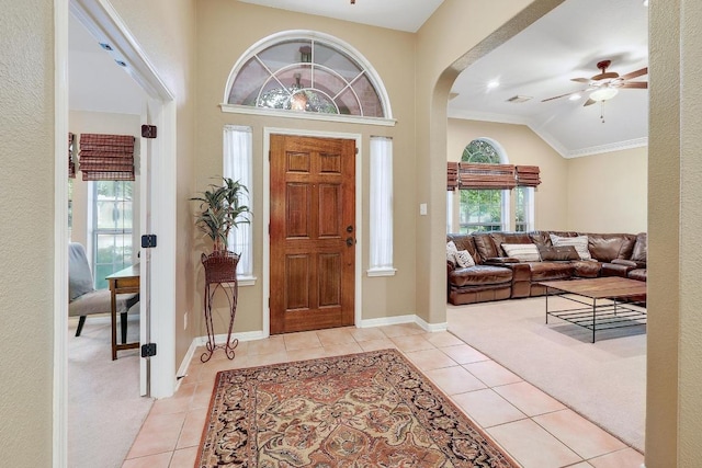 entrance foyer with a ceiling fan, crown molding, arched walkways, light tile patterned floors, and baseboards
