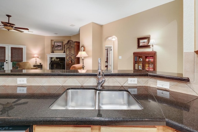 kitchen with a ceiling fan, a fireplace, open floor plan, arched walkways, and a sink