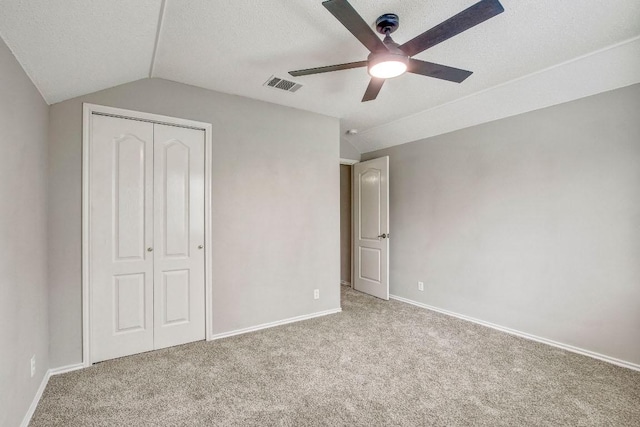 unfurnished bedroom featuring carpet floors, baseboards, lofted ceiling, visible vents, and a closet
