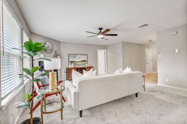 living area with visible vents, baseboards, light colored carpet, a textured ceiling, and a ceiling fan