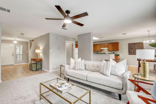 living room featuring ceiling fan with notable chandelier, a textured ceiling, and visible vents