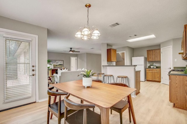 dining space with light wood-style floors, baseboards, ceiling fan with notable chandelier, and visible vents
