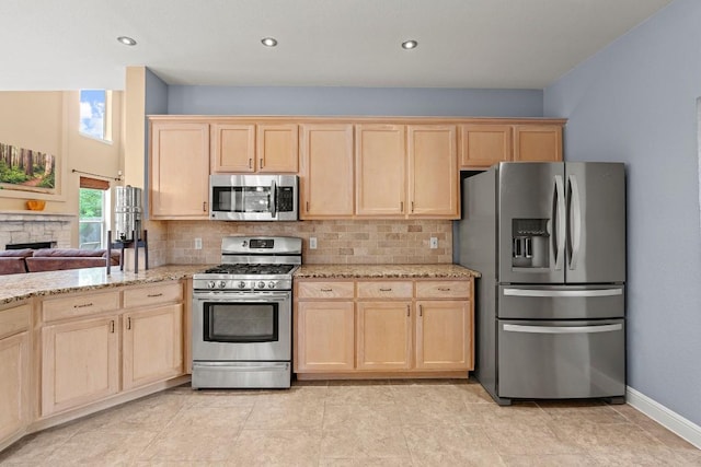 kitchen with backsplash, appliances with stainless steel finishes, light brown cabinetry, and light stone countertops