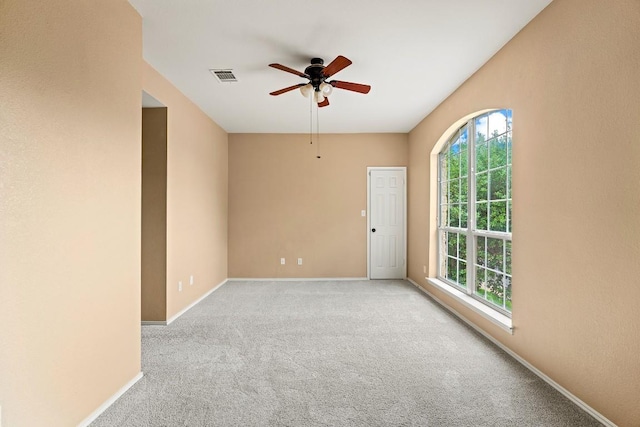 carpeted empty room with baseboards, ceiling fan, visible vents, and a wealth of natural light