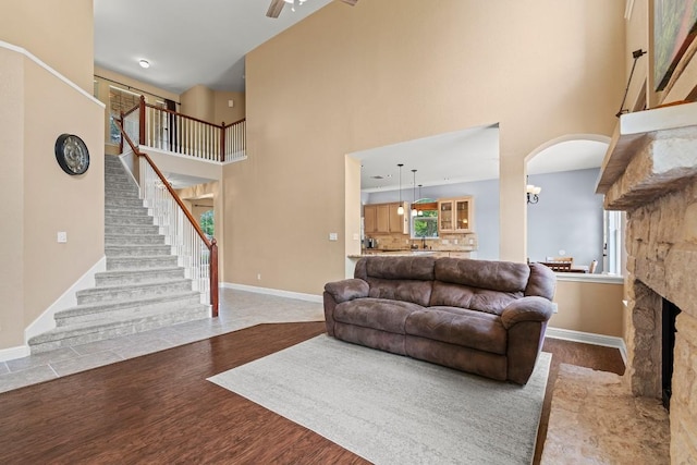 living room with wood finished floors, baseboards, a stone fireplace, a high ceiling, and stairway