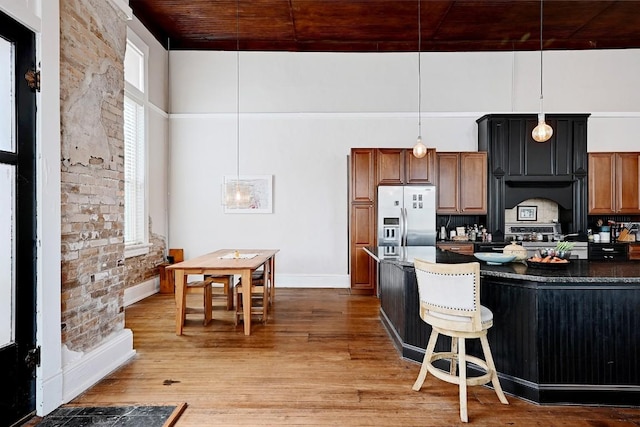 kitchen with wood finished floors, dark countertops, a high ceiling, stainless steel fridge, and hanging light fixtures