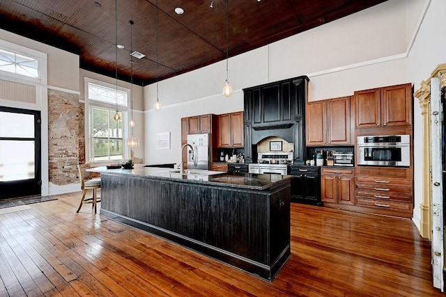 kitchen with a large island, hardwood / wood-style flooring, a sink, a high ceiling, and stainless steel appliances