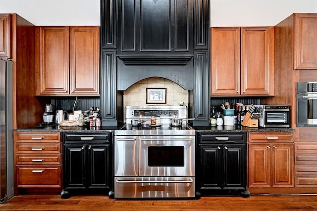 kitchen featuring a toaster, dark stone countertops, stainless steel appliances, dark wood-type flooring, and backsplash