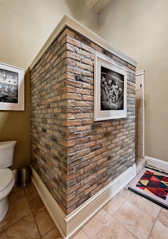 bathroom featuring baseboards, tile patterned floors, toilet, and brick wall