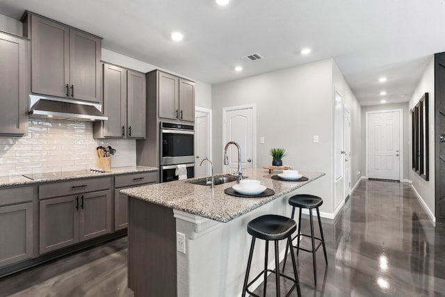 kitchen with visible vents, decorative backsplash, double oven, under cabinet range hood, and a sink