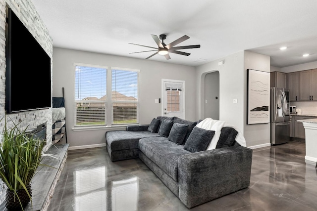 living area with arched walkways, ceiling fan, baseboards, and concrete floors