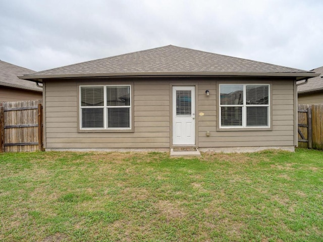 back of house with a lawn, fence, and a shingled roof