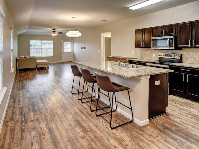kitchen featuring a sink, a kitchen breakfast bar, light wood-style flooring, stainless steel appliances, and decorative backsplash