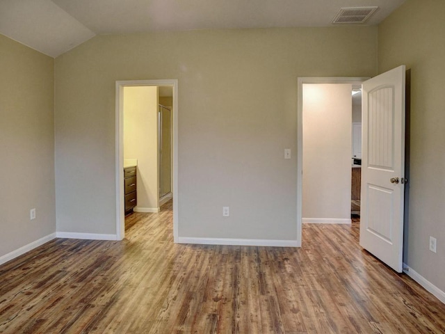 unfurnished bedroom with visible vents, baseboards, lofted ceiling, and wood finished floors