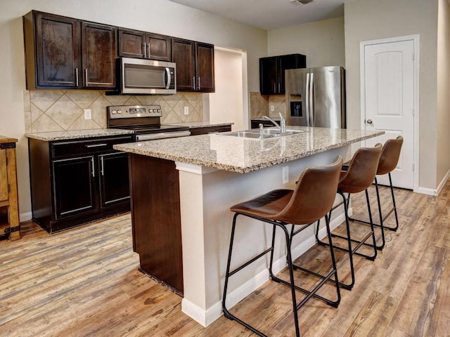 kitchen with a sink, light wood-style flooring, a kitchen bar, and stainless steel appliances
