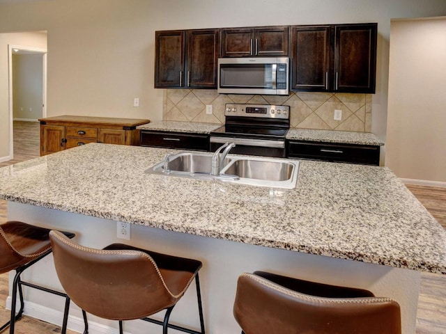 kitchen with decorative backsplash, appliances with stainless steel finishes, light wood-type flooring, a sink, and baseboards