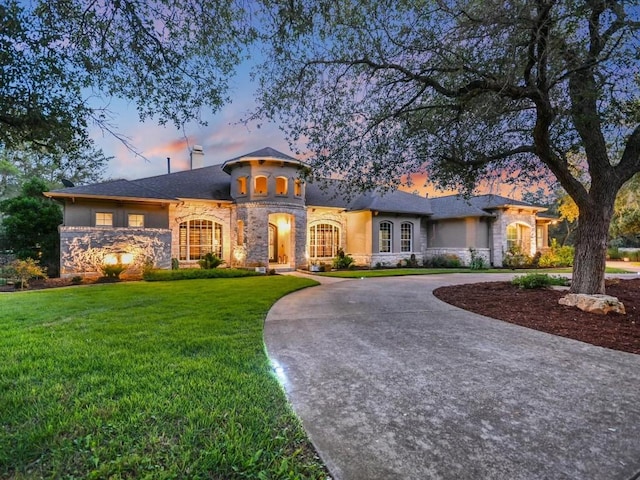 view of front of house featuring a lawn, curved driveway, stone siding, and stucco siding