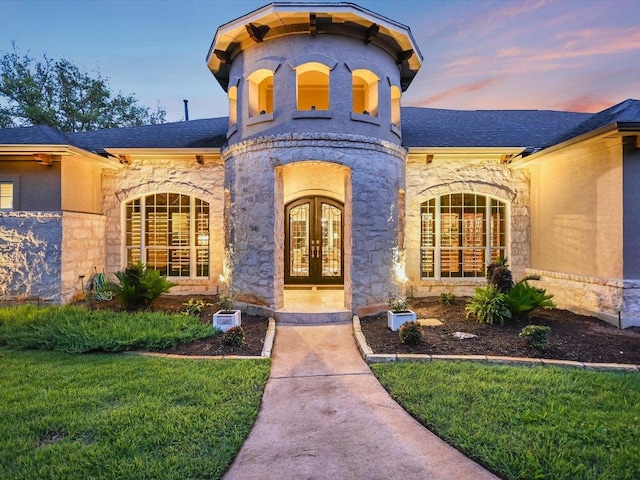 exterior entry at dusk featuring a lawn, a shingled roof, french doors, and stone siding