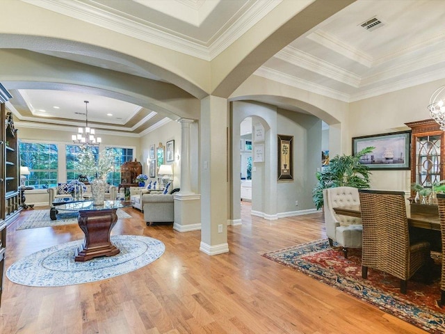 entryway featuring an inviting chandelier, a raised ceiling, arched walkways, light wood-style flooring, and visible vents
