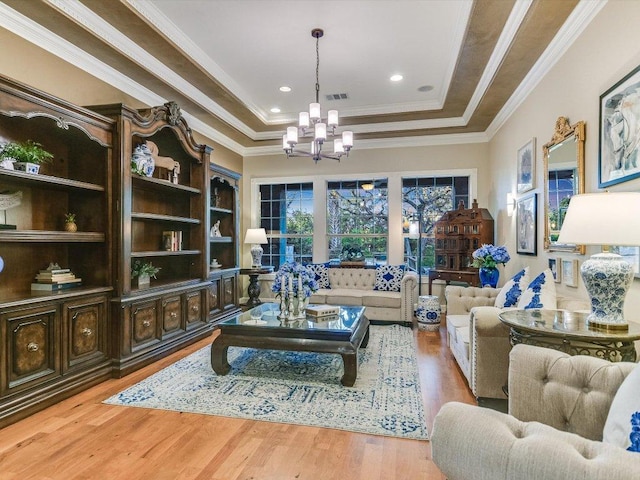 living area with visible vents, ornamental molding, wood finished floors, a raised ceiling, and a notable chandelier