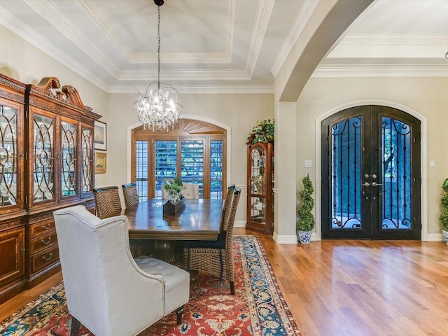 dining space featuring arched walkways, a chandelier, french doors, wood finished floors, and a tray ceiling