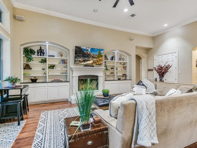 5709 Laguna Cliff Ln, Austin, TX 78734 - living area featuring light wood-style floors, a fireplace with raised hearth, built in shelves, a ceiling fan, and crown molding