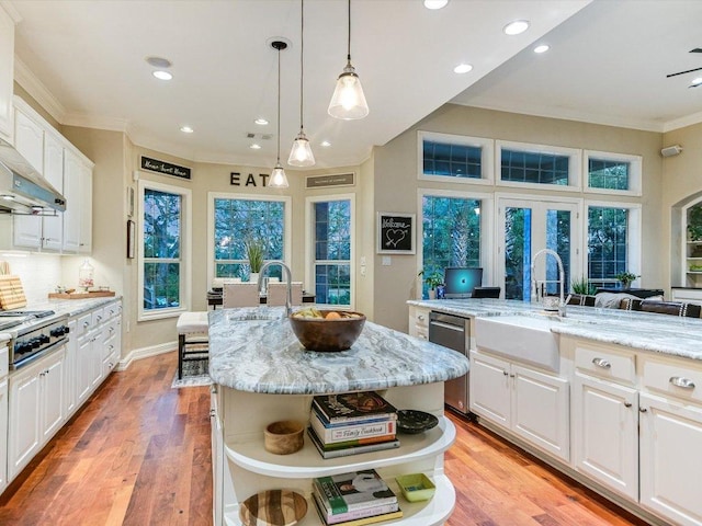 kitchen featuring a kitchen island with sink, crown molding, appliances with stainless steel finishes, open shelves, and a sink