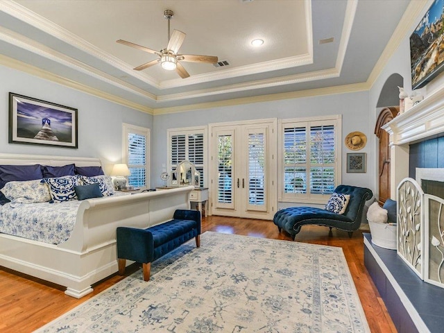bedroom featuring access to exterior, crown molding, wood finished floors, a fireplace with raised hearth, and a tray ceiling