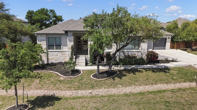 view of property hidden behind natural elements featuring driveway, fence, a front lawn, an attached garage, and stone siding