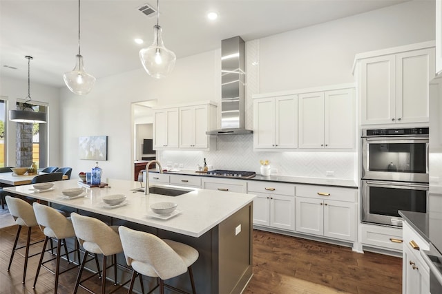 kitchen with wall chimney range hood, decorative backsplash, visible vents, a sink, and stainless steel appliances