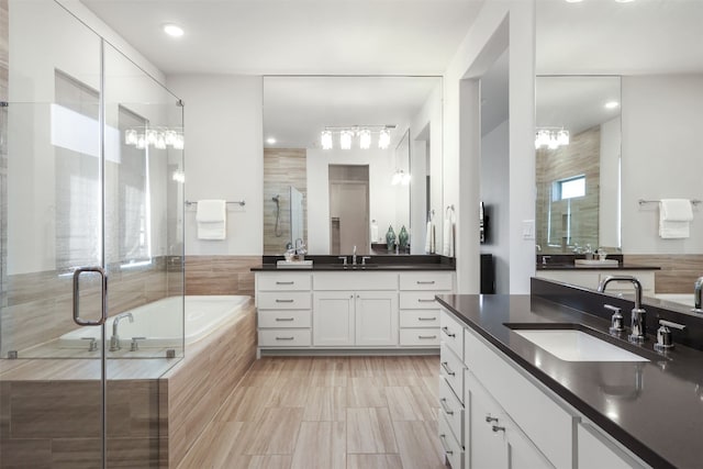 full bathroom with two vanities, a sink, a bath, and a stall shower